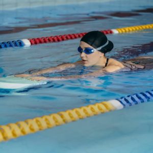 young woman in goggles swims with a board in the pool